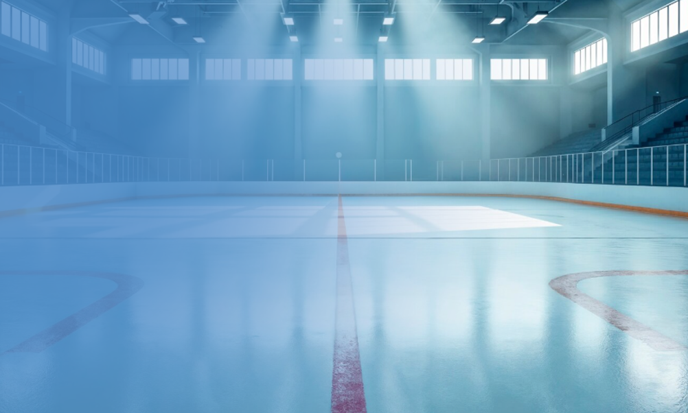 Empty indoor ice hockey rink illuminated by bright natural light from overhead windows.