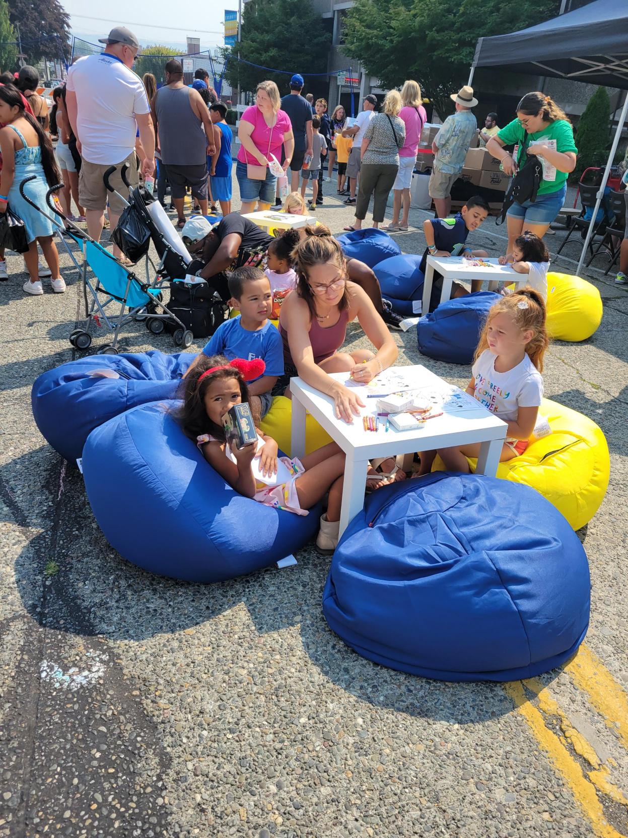 Children Coloring: Children sit outside on colorful blue and yellow bean bag chairs and color in pictures of Freddy Funko at tables. 