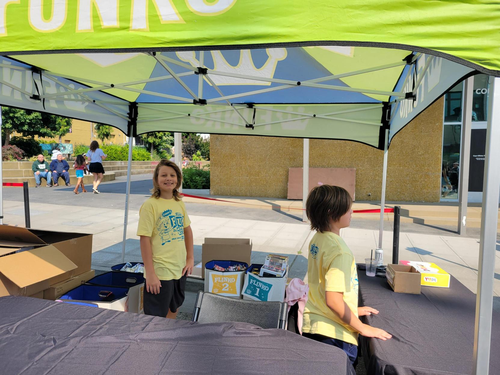 Children Volunteering: Two children, in yellow Fun Fest 2023 tee shirts help staff the “Flinko” tent.